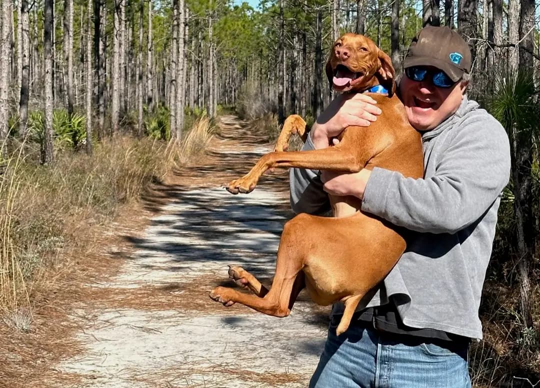Garett holding his dog Buda on a sandy pine-forest trail